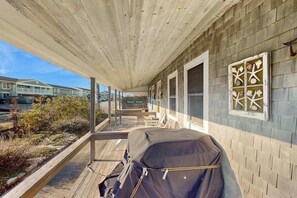 A covered porch with a grill, a bench, and a sign that reads 'BEACH HOUSE.'