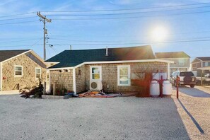 A single-story building with a gravel driveway, a small garden area, and a parked vehicle in the background.