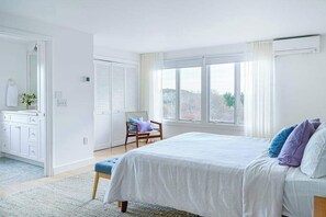 Een slaapkamer met een bed, een stoel, een dressoir en een raam met uitzicht.