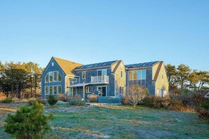 Een groot, twee verdiepingen hoog huis met een opvallend balkon, een voortuin en zonnepanelen op het dak.