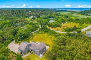 An aerial view of a residential area with houses surrounded by greenery and a clear view of the ocean. - Sun-filled escape with hot tub, deck, bikes, grill, W/D, & Central AC (Truro)