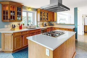 A modern kitchen with wooden cabinets, a central island, and a stove. - Sun-filled escape with hot tub, deck, bikes, grill, W/D, & Central AC (Truro)