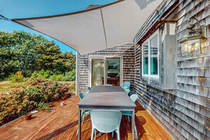 Een houten terras met een tafel en stoelen, een overdekte patio en een huis met raam en deur.