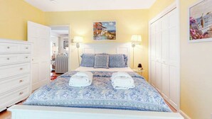 A bedroom with a bed, bedside lamps, a painting, and a wardrobe.