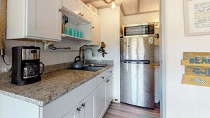 Une cuisine avec des meubles blancs, un réfrigérateur en acier inoxydable, une machine à café et un luminaire suspendu.