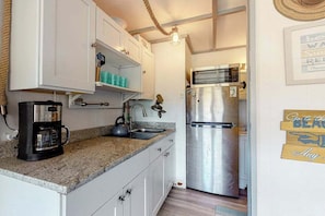 A kitchen with white cabinets, a stainless steel refrigerator, a coffee maker, and a hanging light fixture.