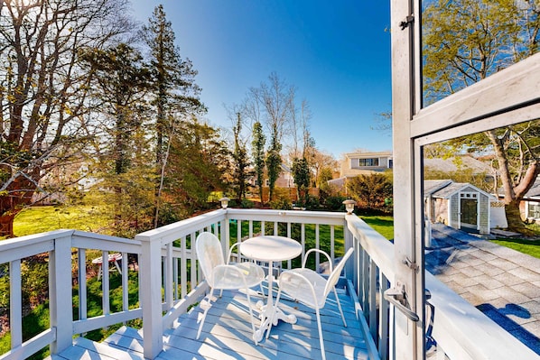 A deck with a table and chairs, surrounded by trees and a lawn.