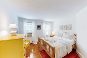 A bedroom with a wooden bed, a yellow dresser, a bedside table with a lamp, and a window with curtains.