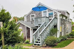 A two-story house with a staircase leading to a balcony, surrounded by greenery.
