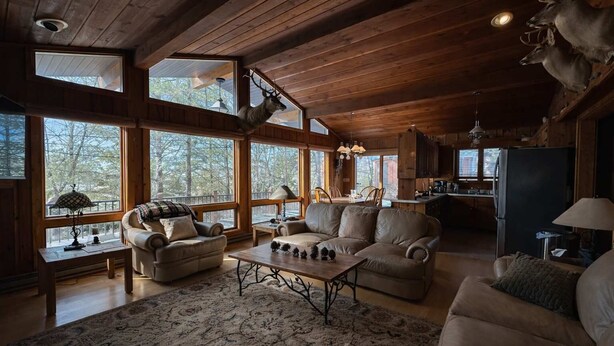 A cozy cabin interior with a fireplace, large windows, a dining area, and a kitchen. - Stack's Back Bay Retreat (Minocqua)