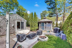 Un jardin avec un patio couvert, un belvédère, un barbecue et un foyer extérieur.
