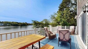 A deck with a wooden table and chairs, overlooking a body of water. - Waterfront gem with deck, bonus den & 2 kayaks - near dining & beach (South Yarmouth)