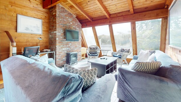 A cozy cabin interior with a brick fireplace, wooden ceiling beams, a television, and a comfortable seating area. - Waterfront gem with deck, bonus den & 2 kayaks - near dining & beach (South Yarmouth)
