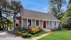 A single-story house with a red front door, a small porch, and a flag. - Waterfront gem with deck, bonus den & 2 kayaks - near dining & beach (South Yarmouth)