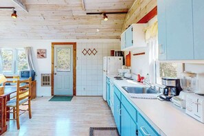 A kitchen with wooden cabinets, a sink, and a dining area with a table and chairs. - Charming Private Truro Cottage with Deck Near Bay Beaches (Truro)