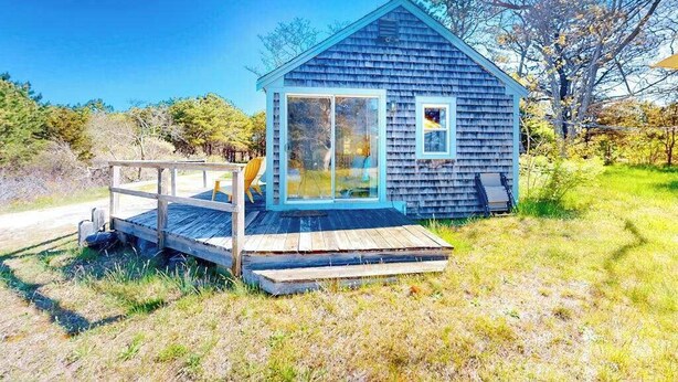 A small wooden cabin with a deck, large windows, and a clear view of the surrounding landscape.