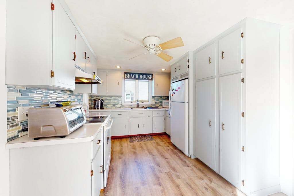 Eine Küche mit weißen Schränken, einem Deckenventilator, einem Toaster und einem Schild mit der Aufschrift 'BEACH HOUSE'.