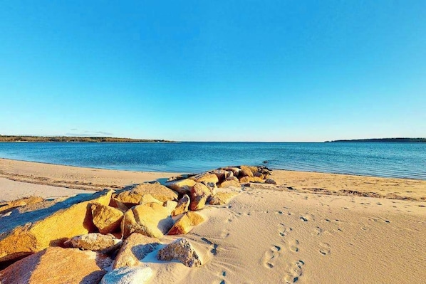 Una playa con grandes rocas al frente y un cielo azul despejado.