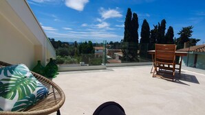 Ein Balkon mit Korbstuhl, Holzstuhl und Blick auf die umliegende Landschaft.
