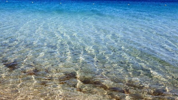 Freie Sicht auf das Meer mit erkennbaren Felsen unter der Wasseroberfläche und ruhiger Meeresoberfläche.