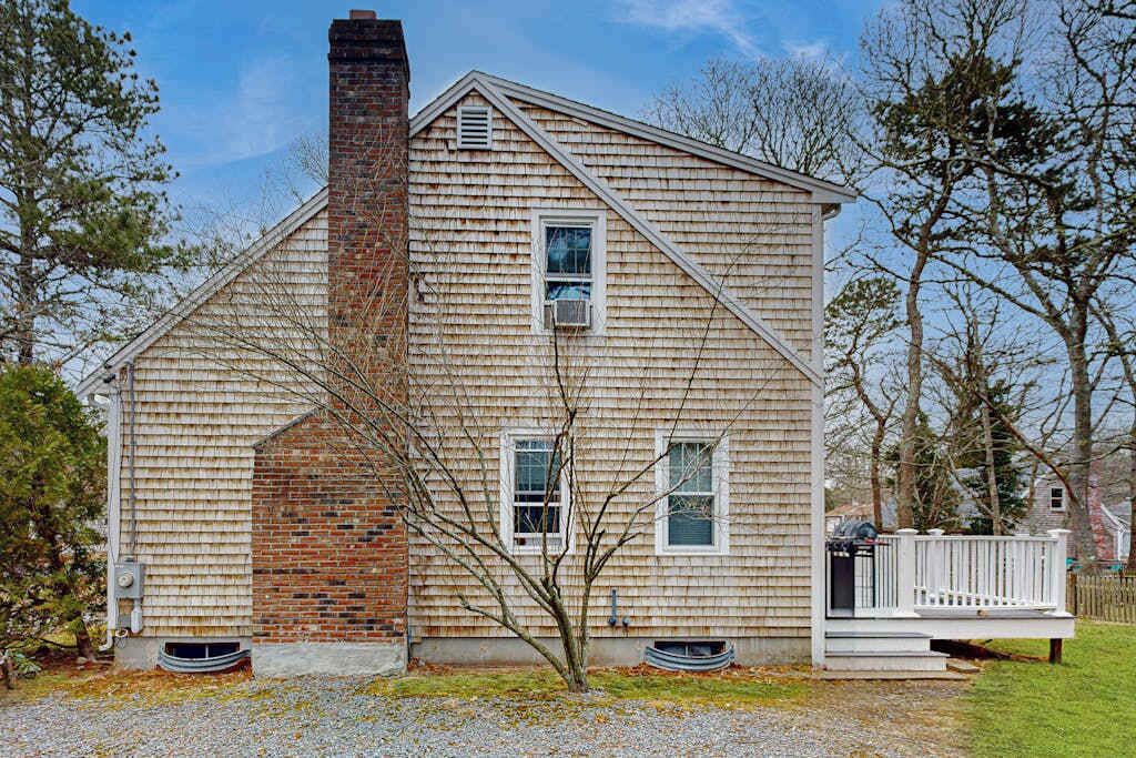 A single-story house with a brick chimney, a front porch with a white railing, and a small tree in front.