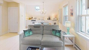 A living room with a sofa, a coffee table, a TV, and a kitchen in the background. - Charming apartment in the heart of town with quick WiFi (Provincetown)