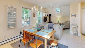 A dining area with a wooden table and chairs, a kitchen in the background, and a living area with a sofa and a TV. - Charming apartment in the heart of town with quick WiFi (Provincetown)