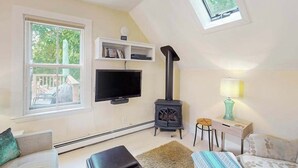 A cozy room with a TV, a fireplace, a window, and a skylight. - Charming apartment in the heart of town with quick WiFi (Provincetown)