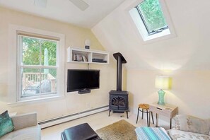 Ein gemütliches Zimmer mit Fernseher, Kamin, Fenster und Dachfenster.
