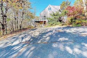 A rustic wooden building with a porch, surrounded by trees and a paved driveway.