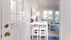 Um quarto com porta branca, uma mesa de jantar com duas cadeiras, um abajur e um sofá.