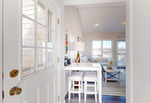 A room with a white door, a dining table with two chairs, a lamp, and a sofa. - Two-story condo with ocean views, parking, & private balcony (Provincetown)