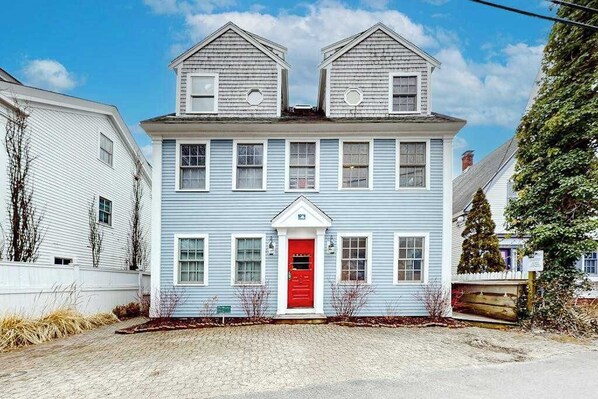 A two-story house with a red front door, white trim, and a small porch. - Updated condo with ocean view, viewing deck, & private W/D (Provincetown)