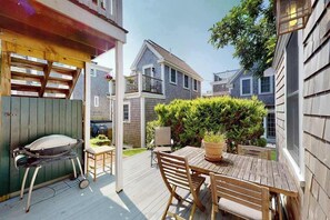 Een houten terras met een tafel, stoelen, een barbecue en een bloempot.