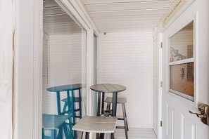 A covered porch with a white door, a small round table, and two blue chairs. - Beautiful condo near the ocean with heated pool, hot tub, grills and kitchenette (Provincetown)