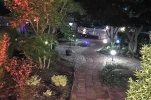 A nighttime garden pathway with illuminated plants and a bicycle. - Beautiful condo near the ocean with heated pool, hot tub, grills and kitchenette (Provincetown)