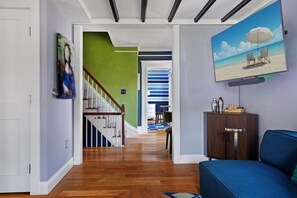 A modern living room with a wooden floor, a blue sofa, a TV mounted on the wall, and a staircase leading to another room. - Gorgeously redesigned 1830 home in the heart of town - walk everywhere (Provincetown)
