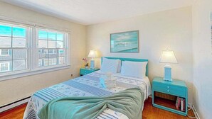 Un dormitorio con una cama, dos mesitas de noche con lámparas, una ventana y un cuadro en la pared.