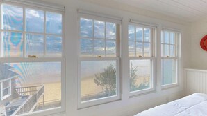 A room with large windows, a bed, and a view of a beach.