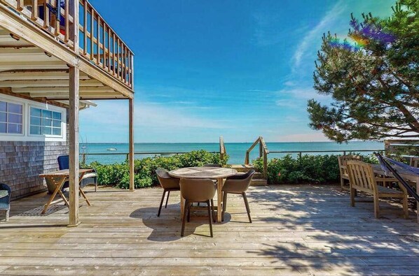 Une terrasse en bois avec une table ronde et des chaises, donnant sur une mer d’un bleu limpide.
