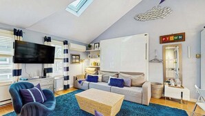 Una sala de estar moderna con un sofá, un televisor, una mesa de centro y un lámpara colgante.