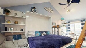 Un dormitorio con cama, sofá, ventilador de techo y ventana con cortinas.