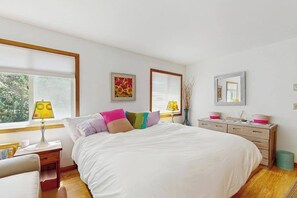 A bedroom with a large bed, bedside tables, a dresser, and a window with blinds.
