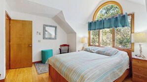 Un dormitorio con cama, ventana con cortinas, puerta de madera y espejo en la pared.