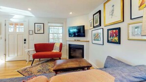 Ein Wohnzimmer mit rotem Sofa, grauem Couchen, Kamin und gerahmten Kunstwerken an der Wand.