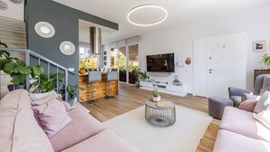 Un soggiorno moderno con un divano, un tavolino, una TV e una scala che conduce a un balcone.