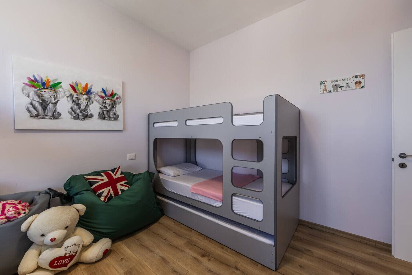 Ein Etagenbett mit grauem Gestell, ein grüner Sitzsack, ein weißer Teddybär und eine Wand mit einem gerahmten Bild.