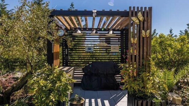 Un giardino con una pergola in legno, un’area relax e piante in vaso.