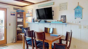 A dining area with a wooden table and chairs, a television on a shelf, and a wall with decorative items.