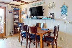 A dining area with a wooden table and chairs, a television on a shelf, and a wall with decorative items.